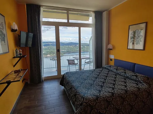 Camera Doppia con Balcone: letto e vista sul Lago d'Orta dalla porta del balcone