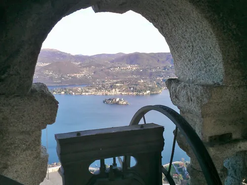 Vista del Lago d'Orta e dell'Isola di San Giulio attraverso l'arco del campanile del Santuario, con la campana in primo piano