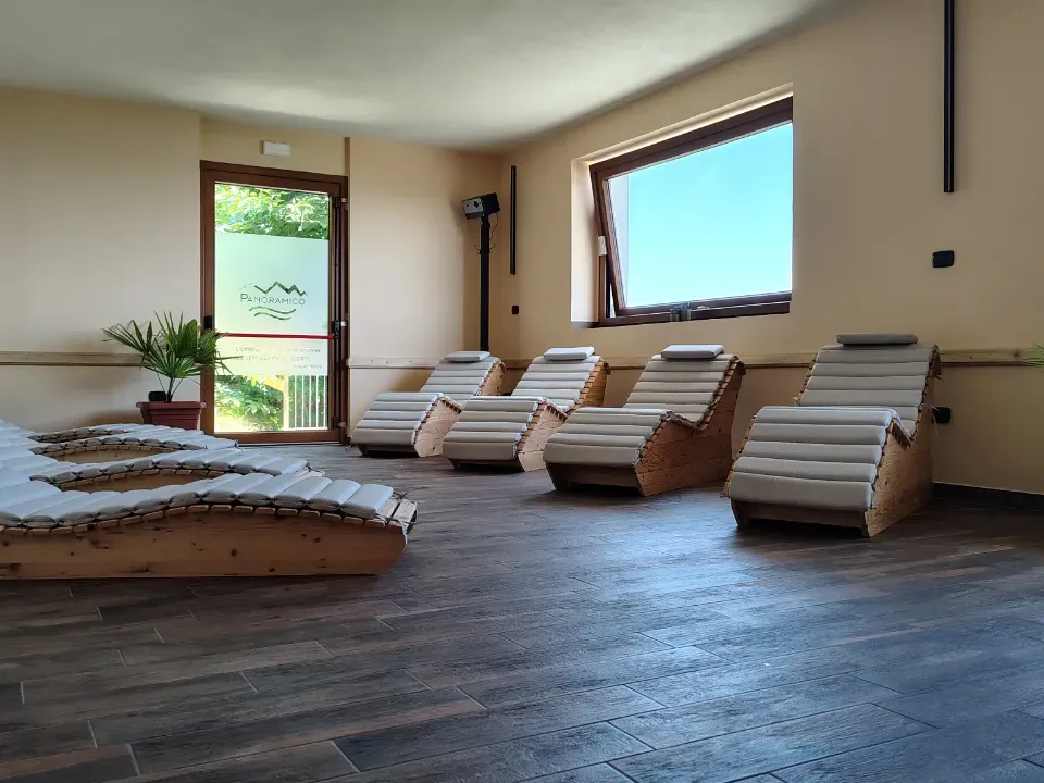 Lettini in legno allineati nella sala relax, con piante e finestra sul verde