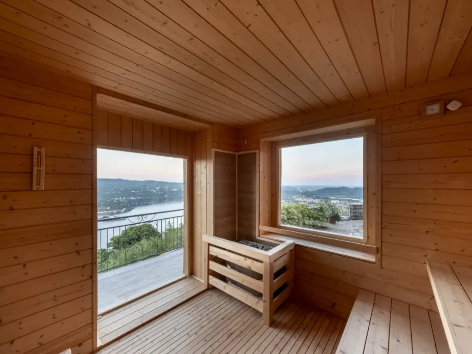 Interno della sauna finlandese in legno, con stufa a pietre e finestra affacciata sul Lago d'Orta