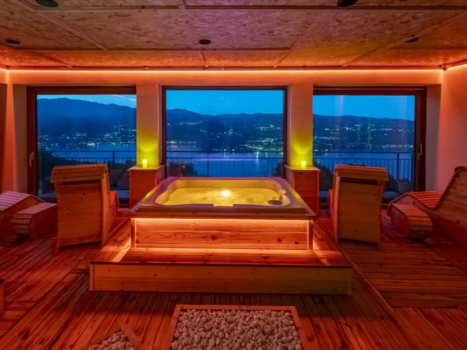 La zona idromassaggio illuminata di rosso al crepuscolo, con le luci del Lago d'Orta oltre le vetrate